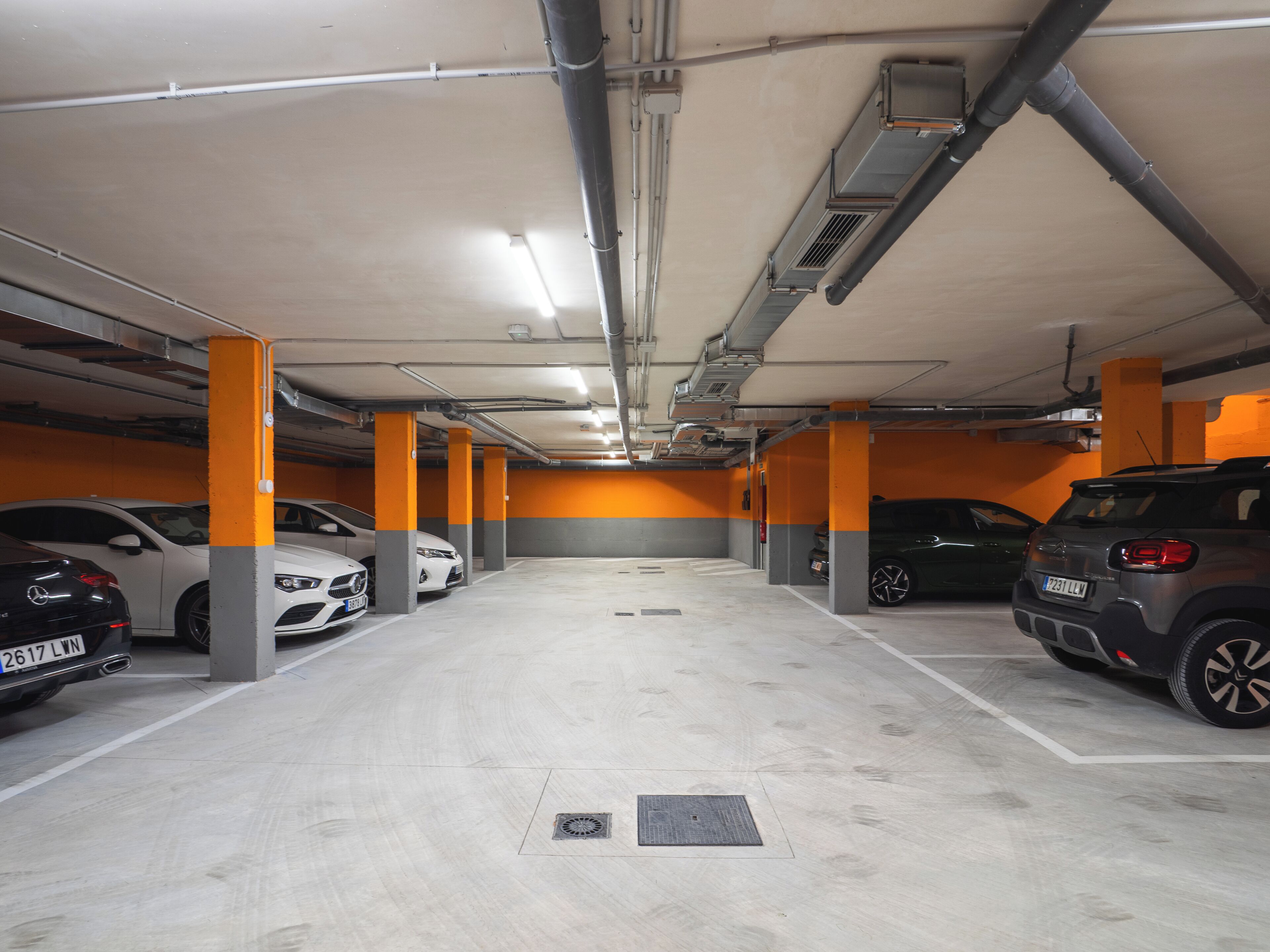 A multi-level parking garage with several cars parked, concrete pillars, and overhead lighting.