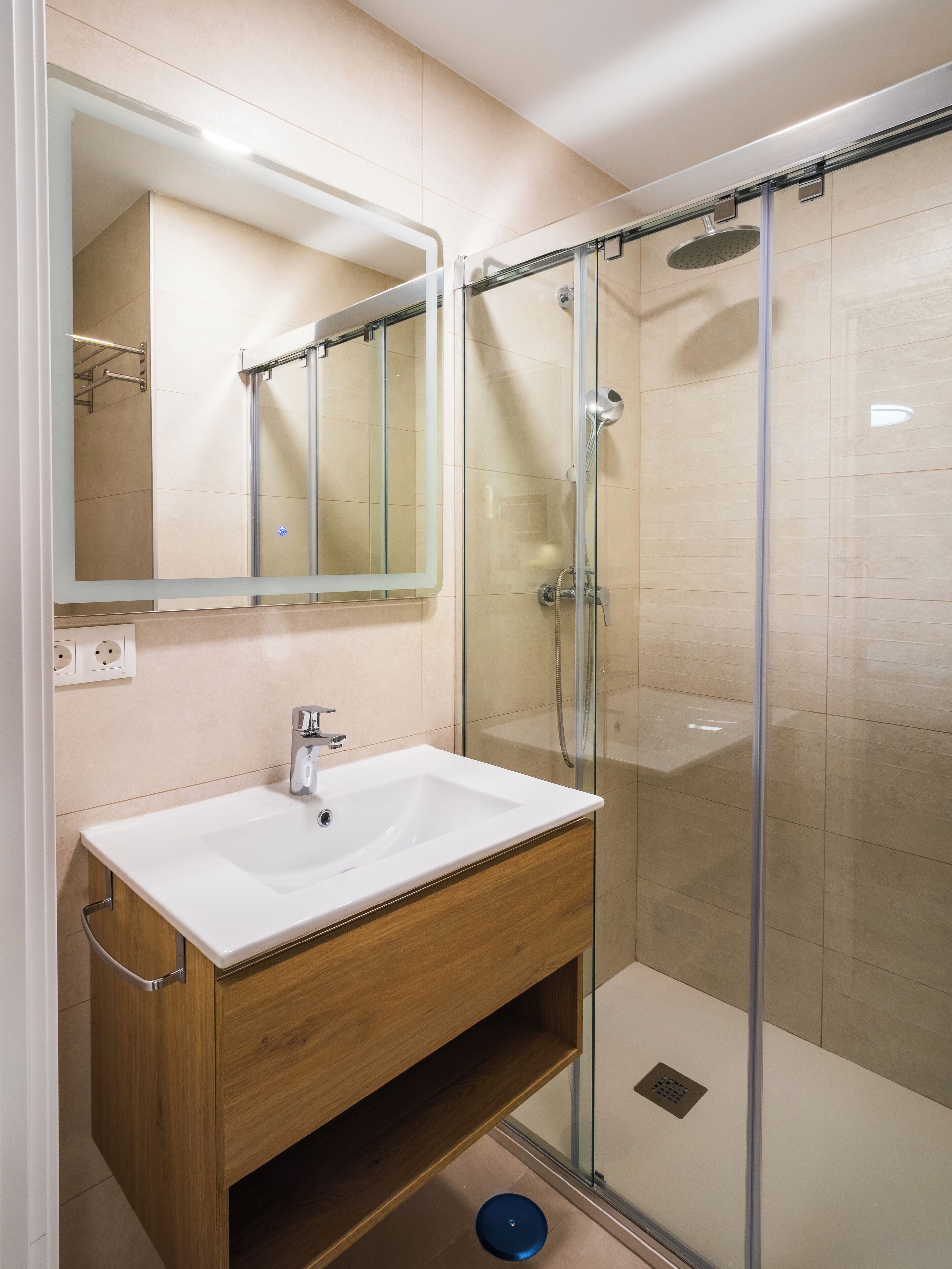 Une salle de bain moderne avec une douche à parois de verre, un lavabo blanc et un meuble-lavabo en bois.