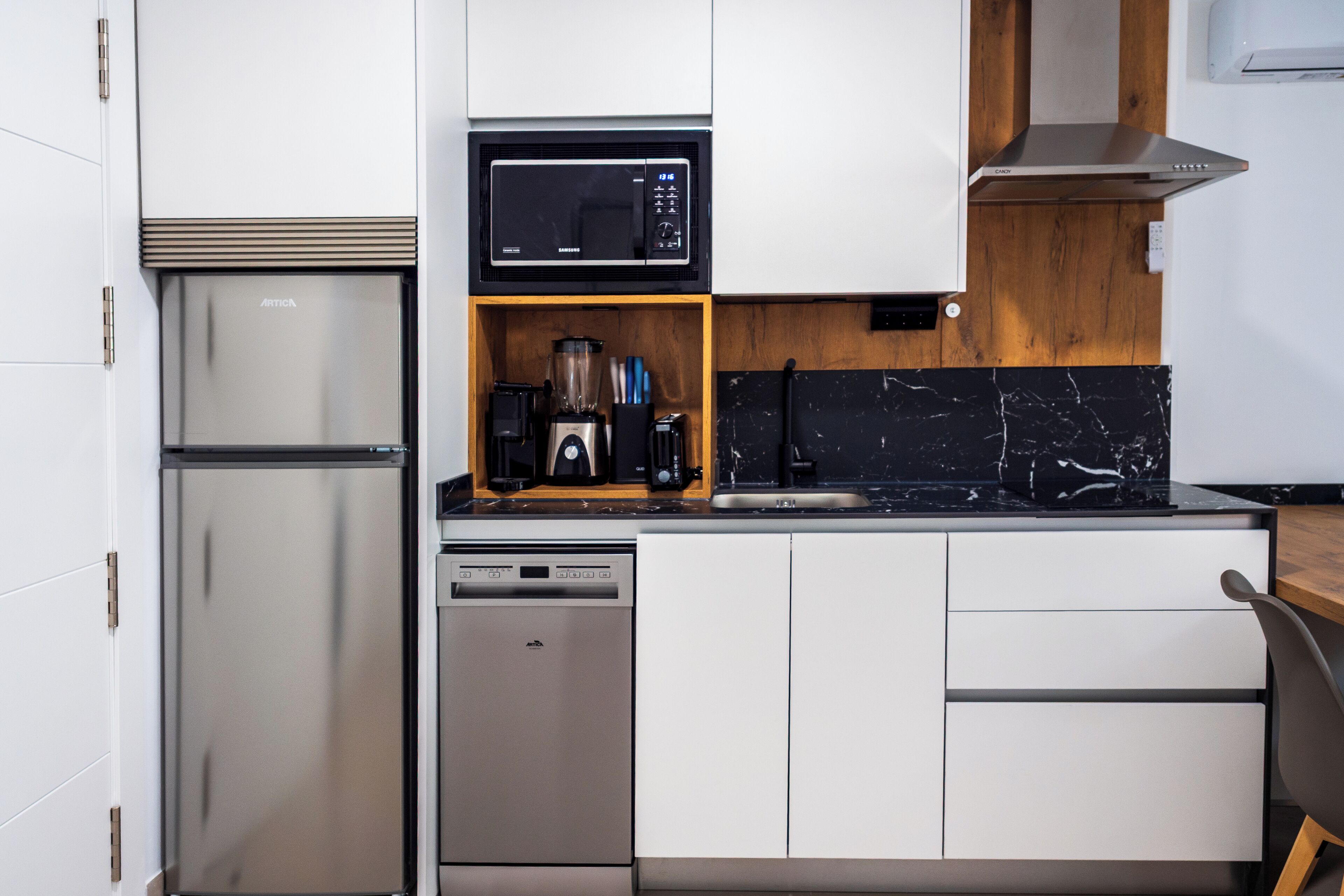 A compact kitchen with a stainless steel refrigerator, a microwave, a built-in blender, and a dishwasher.
