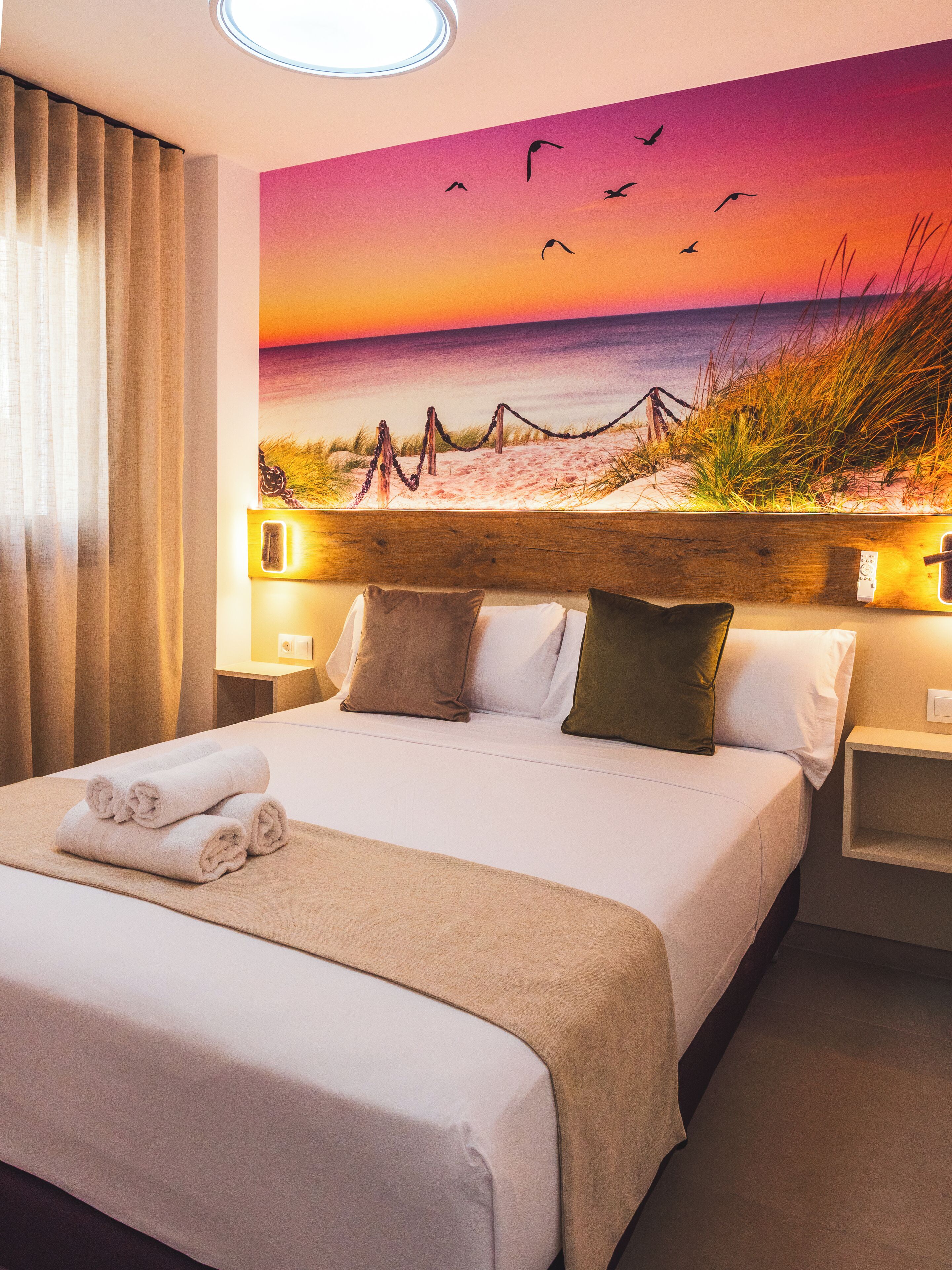 Une chambre d’hôtel avec un grand lit, une tête de lit ornée d’une fresque représentant une plage et une vue sur l’océan.
