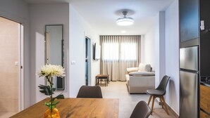Een moderne woonkamer met een houten eettafel, een bank en een keuken met een koelkast.