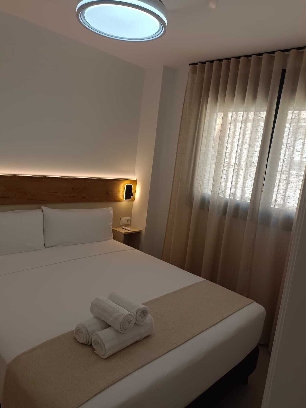 Una habitación de hotel con una cama bien hecha, una lámpara de noche y una ventana con cortinas.