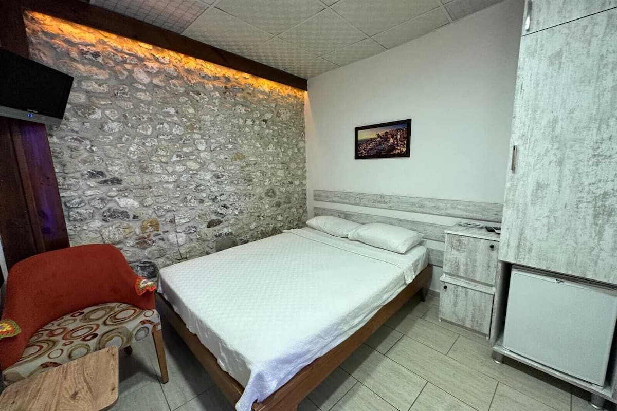 Un dormitorio con pared de piedra, una cama, un televisor, una mesita y un armario.