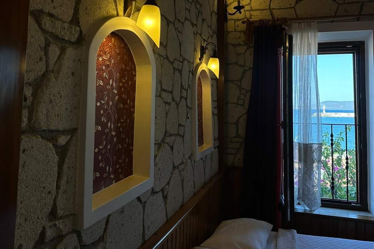 Un dormitorio con paredes de piedra, una cama con ropa blanca y una ventana con vista al mar.