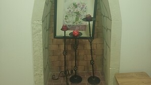 Ein gerahmtes Bild mit Blumen an einer Ziegelwand, ein kleiner Tisch mit Kerzen und ein hölzerner Hocker.