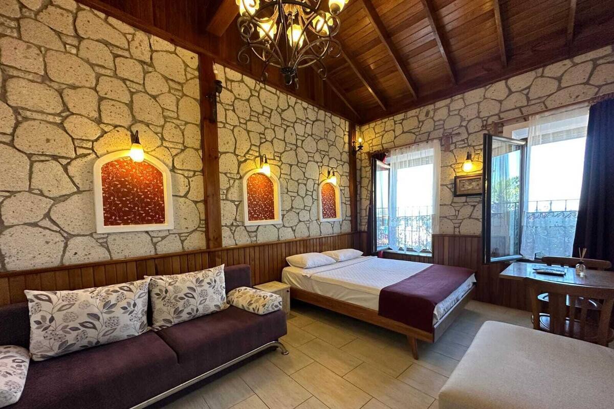 Una habitación con pared de piedra, techo de madera, cama, sofá y una mesa.