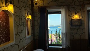 Ein Schlafzimmer mit Steinwand, einem Bett mit weißen Leinentüchern und Meerblick durch ein Fenster.