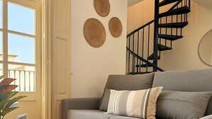 A living room with a grey sofa, a round glass table, a spiral staircase, and decorative wall art.