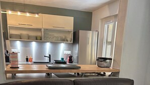 Un salon moderne avec un canapé en cuir foncé, une table basse en bois et un coin cuisine à l’arrière-plan.