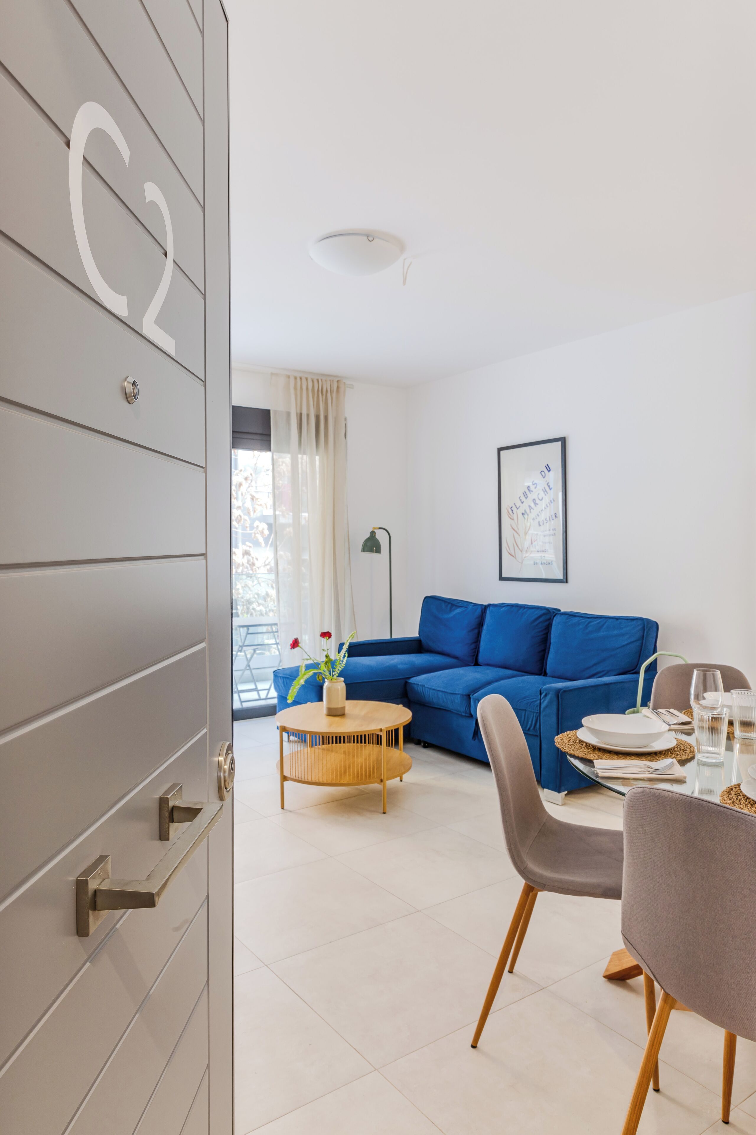 Un salon moderne avec un canapé bleu, une table à manger avec des chaises et une grande fenêtre avec des rideaux.