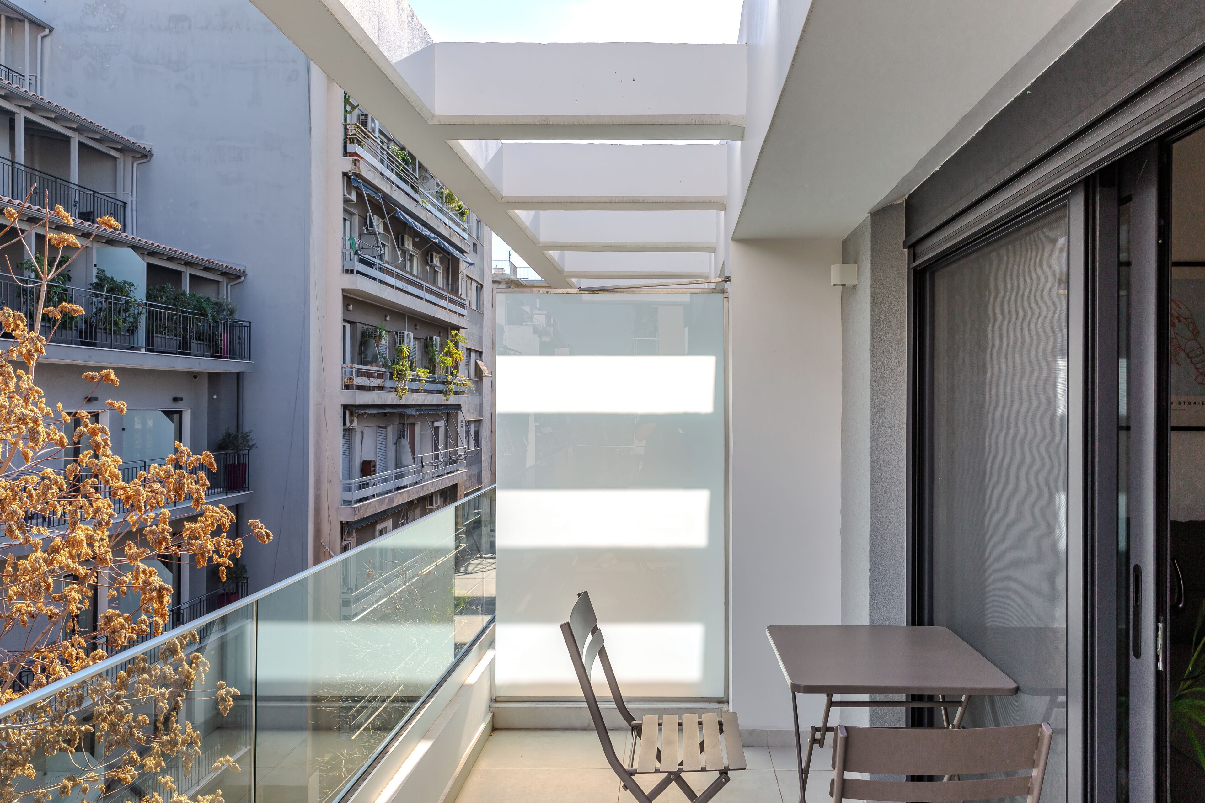 En moderne balkon med gelænder af glas, en træstol og et bord.