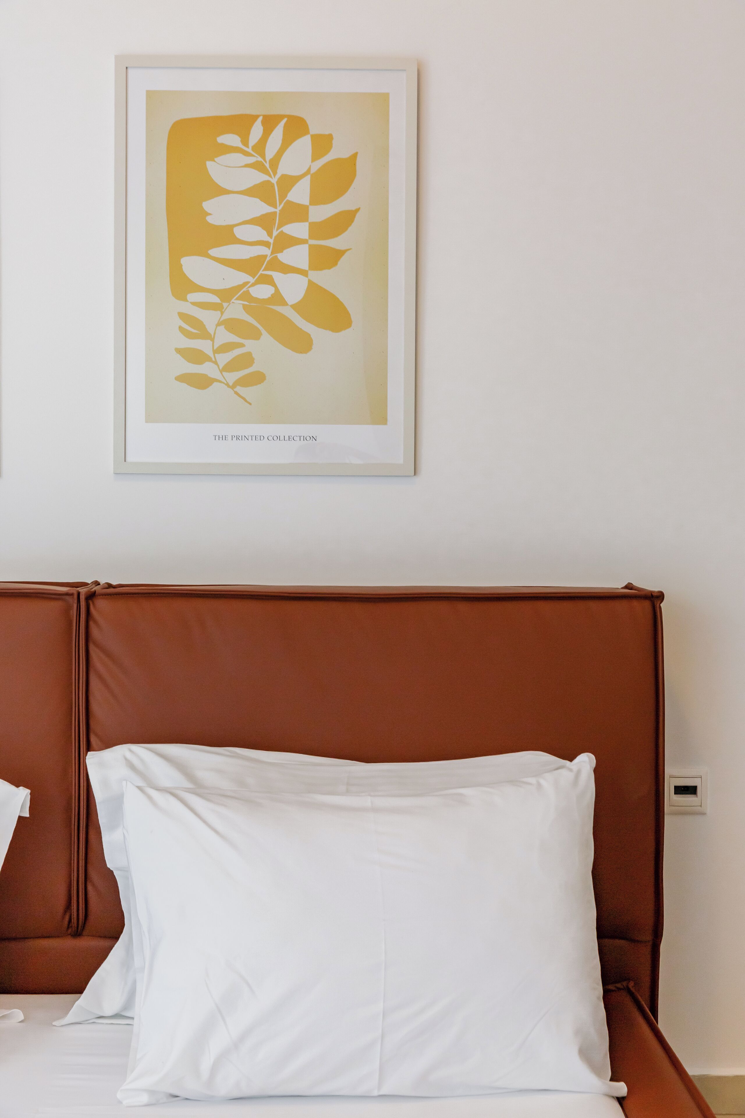 A hotel room with a brown headboard, white bedding, and a framed artwork on the wall.