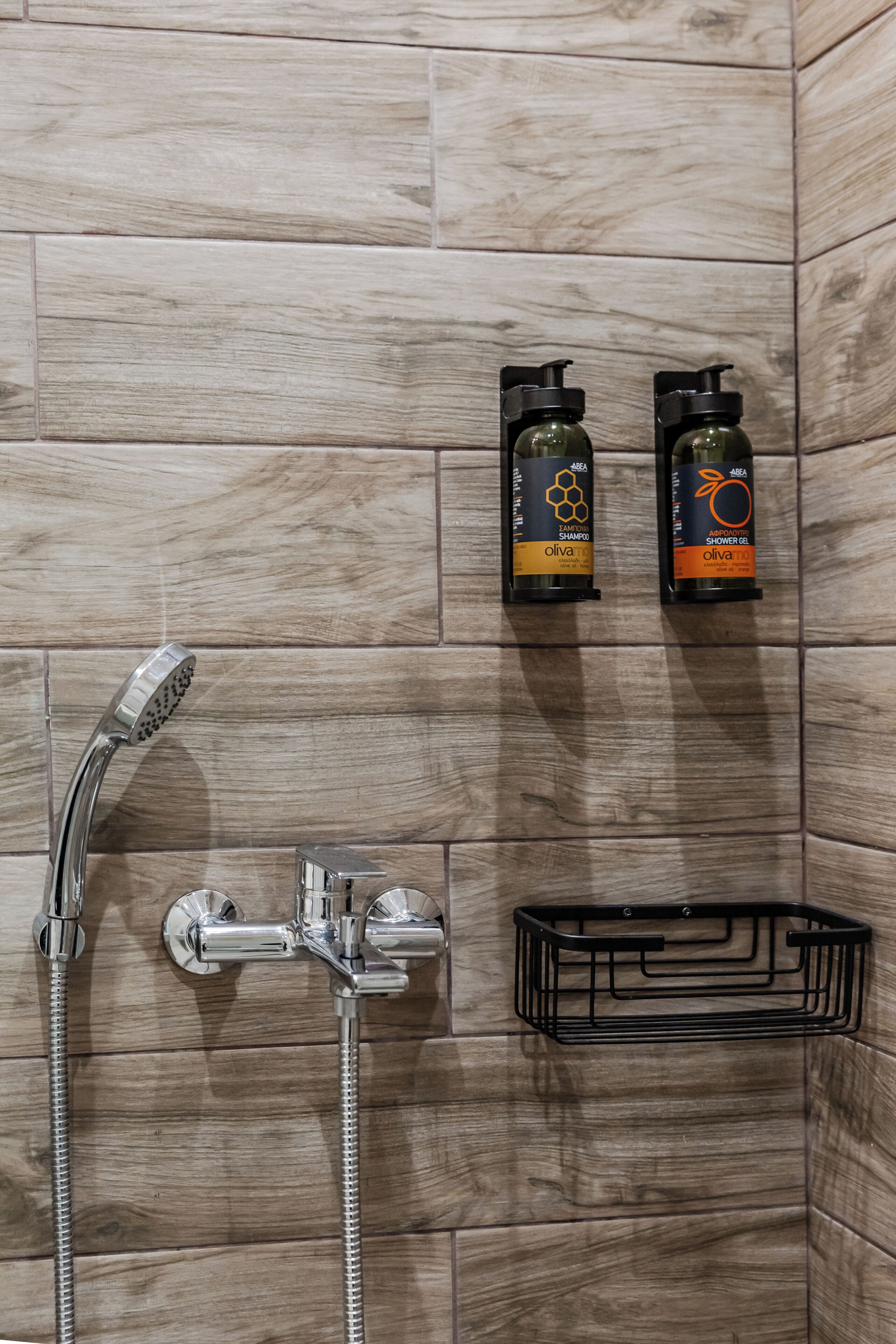 Un baño con ducha, dos botellas de champú y gel de ducha de aceite de oliva, y un perchero metálico negro.