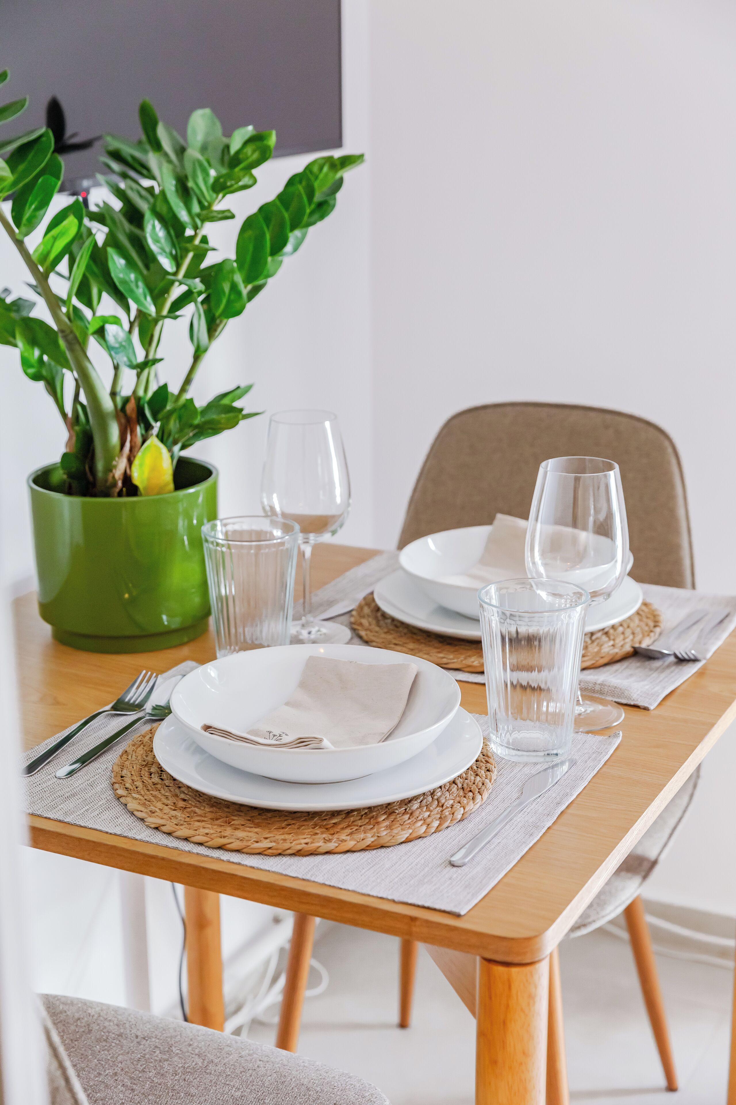 Una mesa de comedor dispuesta con platos, vasos y cubiertos, junto a una planta verde en maceta.