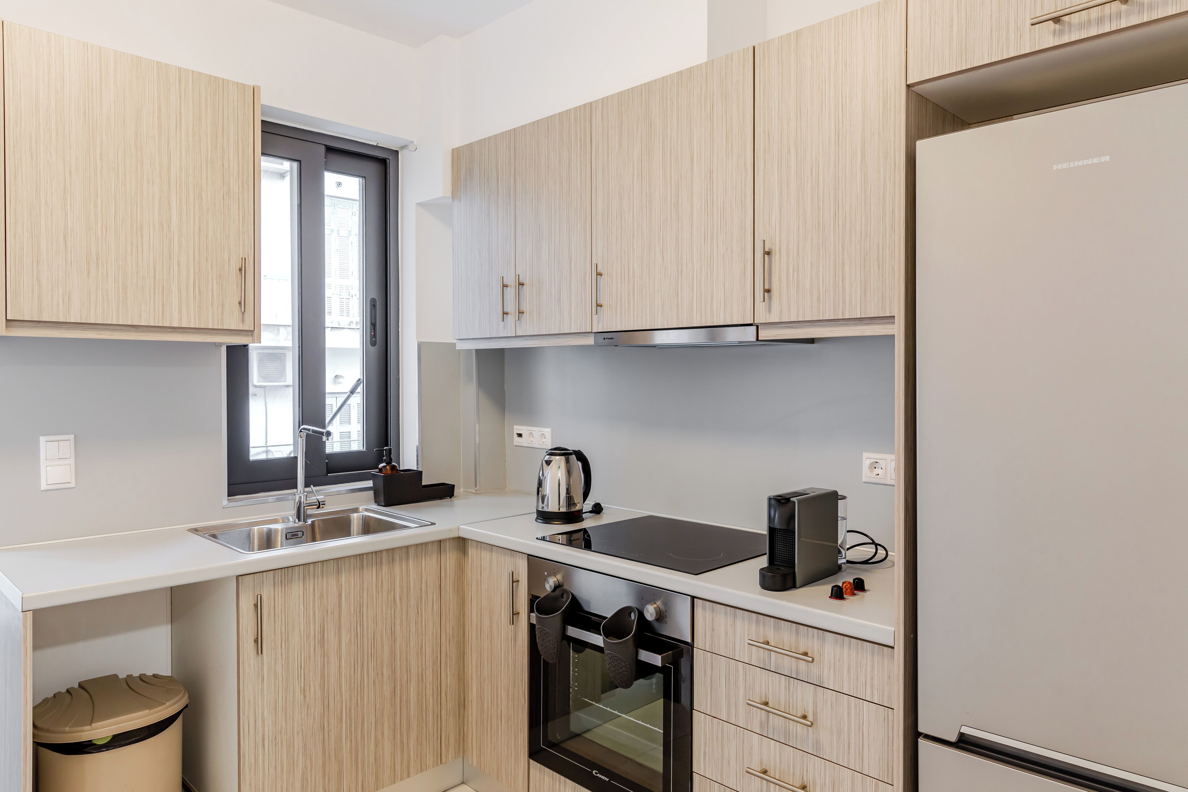 A modern kitchen with light wood cabinets, a stainless steel refrigerator, a built-in oven, and a black countertop.