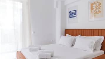 Una cama bien tendida con sábanas y almohadas blancas, un cabecero de madera y dos cuadros en la pared.