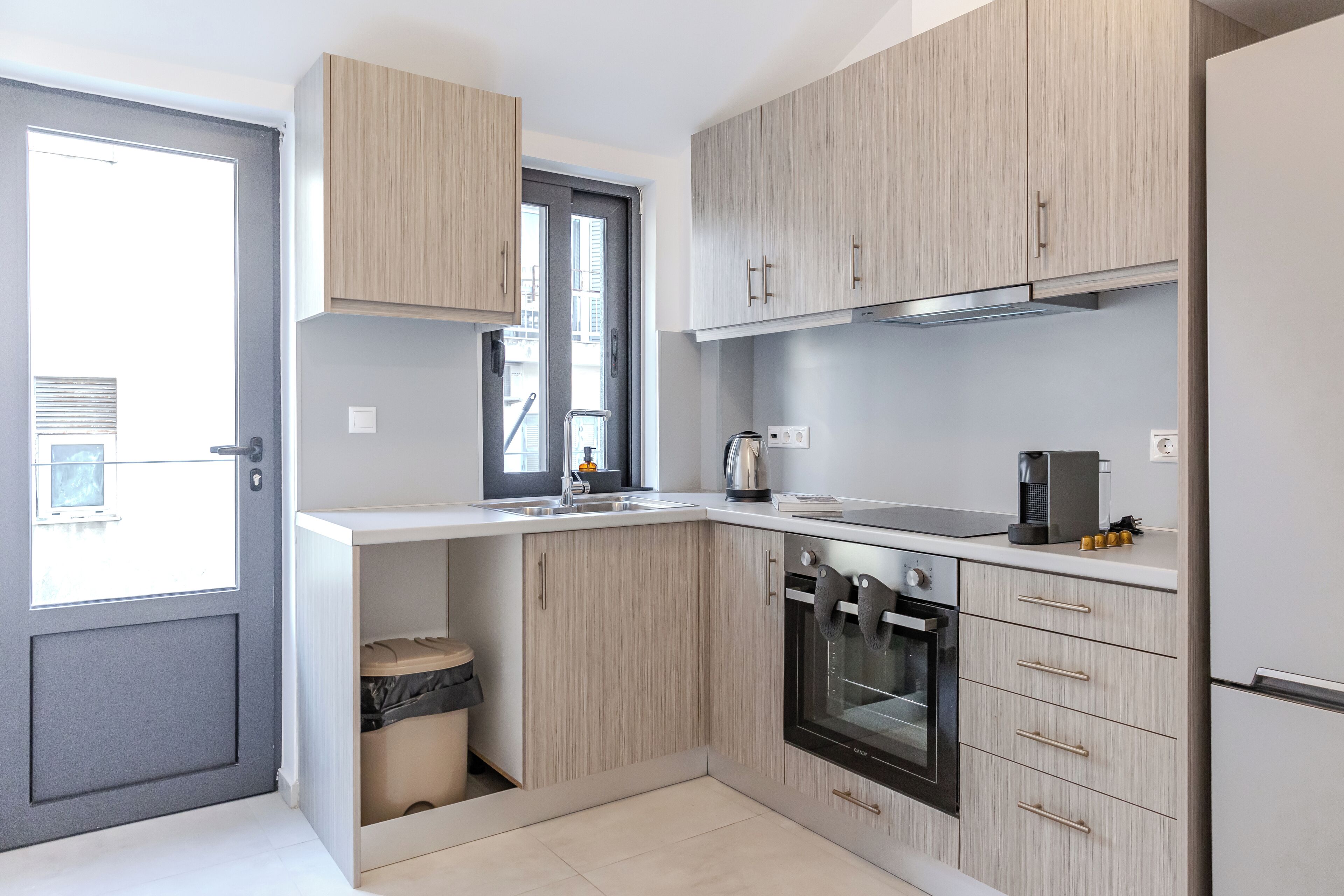 A modern kitchen with light wood cabinets, a built-in oven, and a coffee maker.