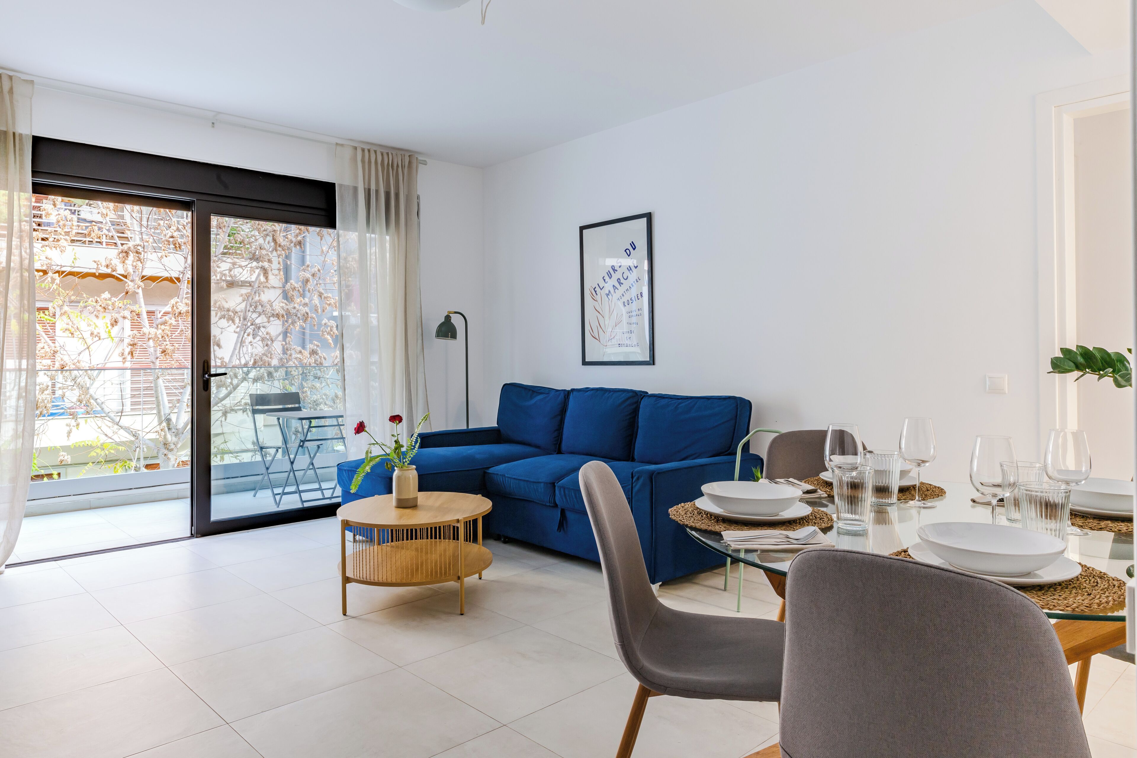 A modern living room with a blue sofa, a dining table set for four, and a sliding glass door leading to a balcony.
