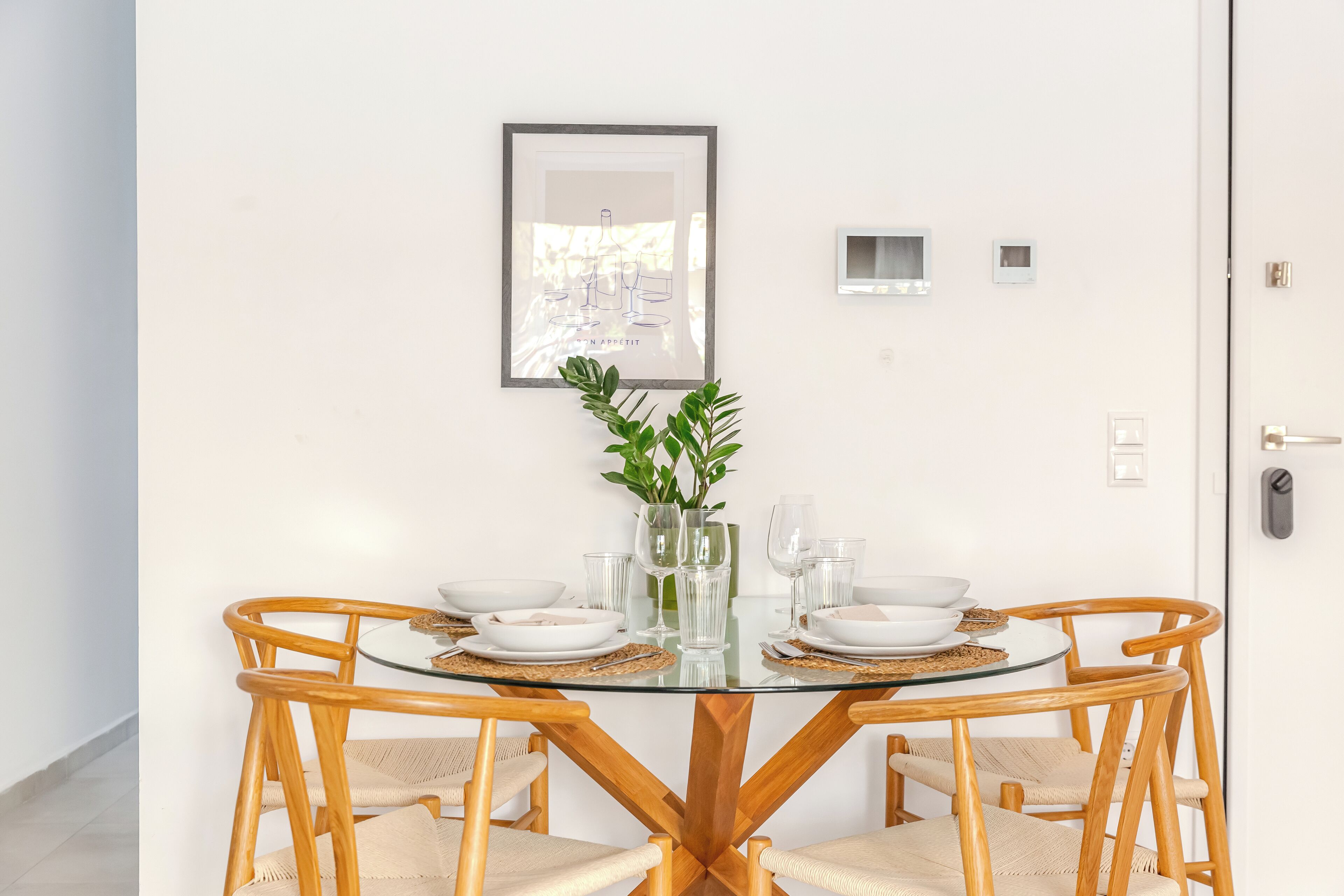 A round glass table with wooden chairs, a framed picture on the wall, and a potted plant.