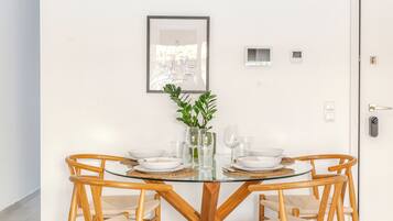 Un tavolo rotondo in vetro con sedie di legno, un quadro incorniciato al muro e una pianta in vaso.
