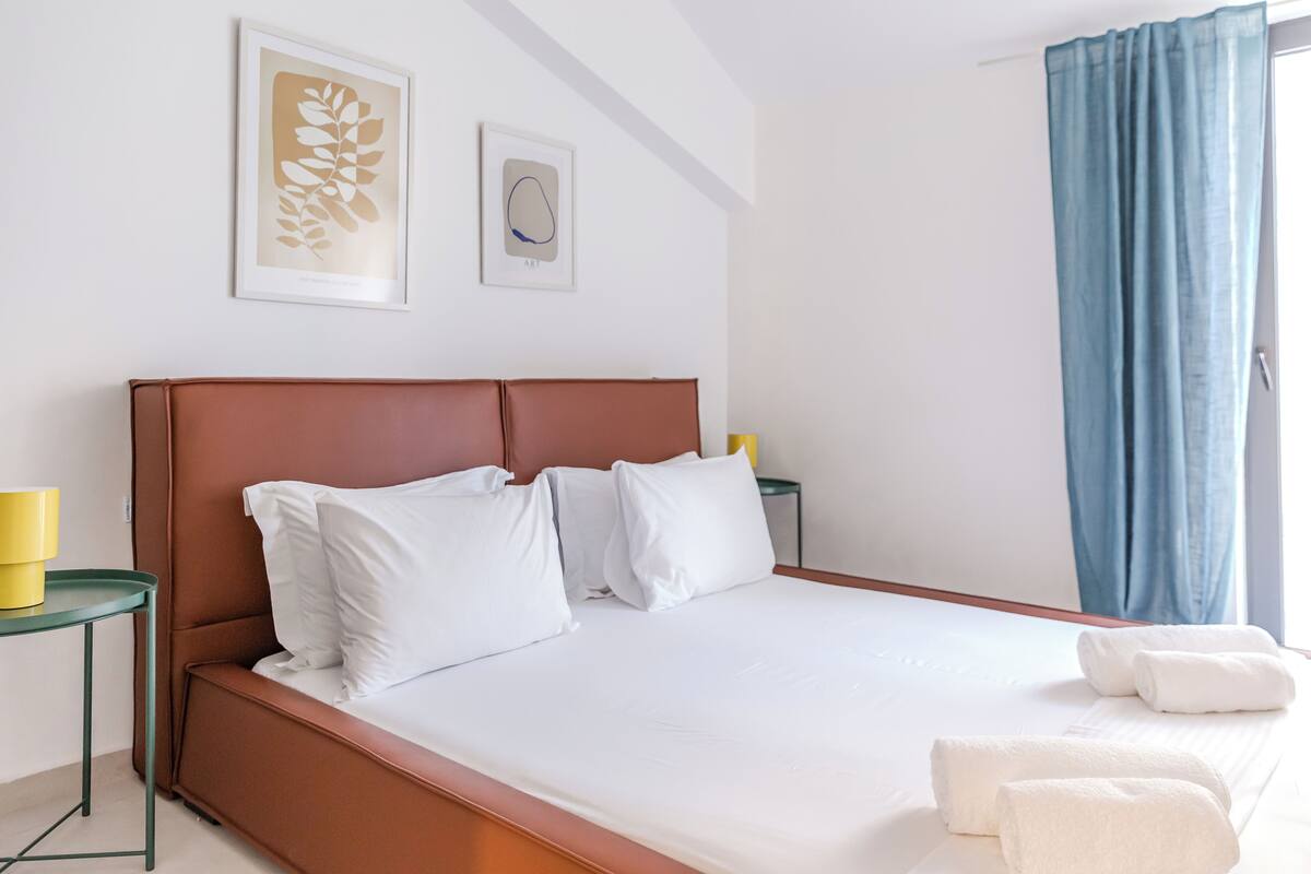 A neatly made bed with white linens, a brown headboard, and two pillows. There are two framed artworks on the wall above the bed.