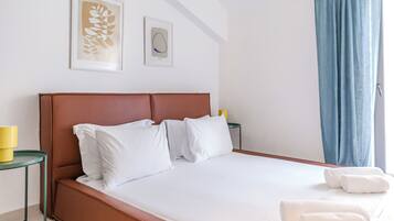 Una cama bien hecha con sábanas blancas, un cabecero marrón y dos almohadas. Hay dos obras de arte enmarcadas en la pared sobre la cama.