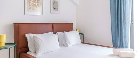 A neatly made bed with white linens, a brown headboard, and two pillows. There are two framed artworks on the wall above the bed.