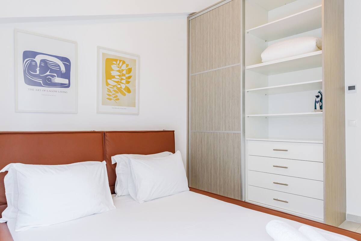 A bedroom with a bed, a wardrobe, and two framed artworks on the wall.