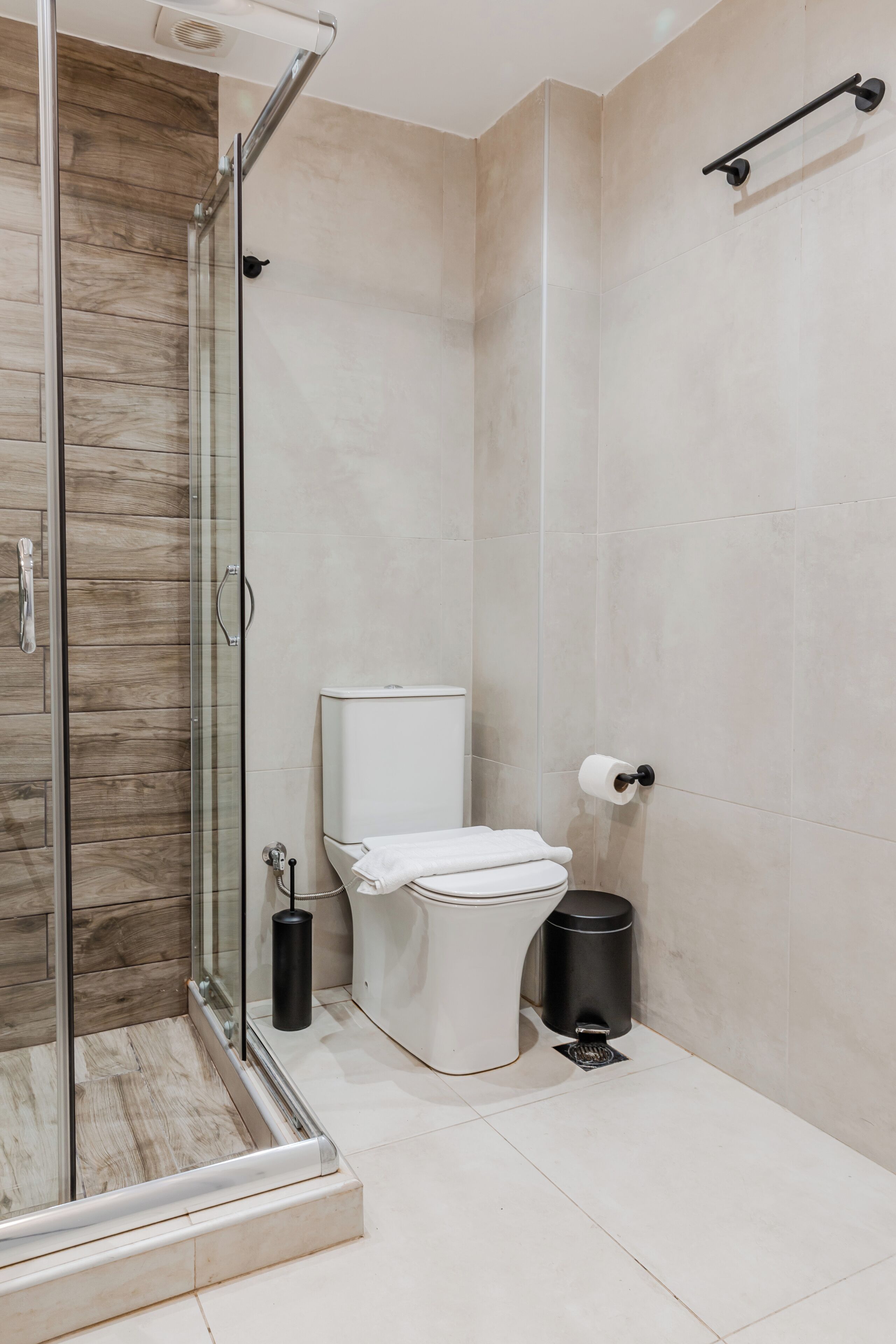 A modern bathroom with a glass shower enclosure, a toilet, and a trash can.