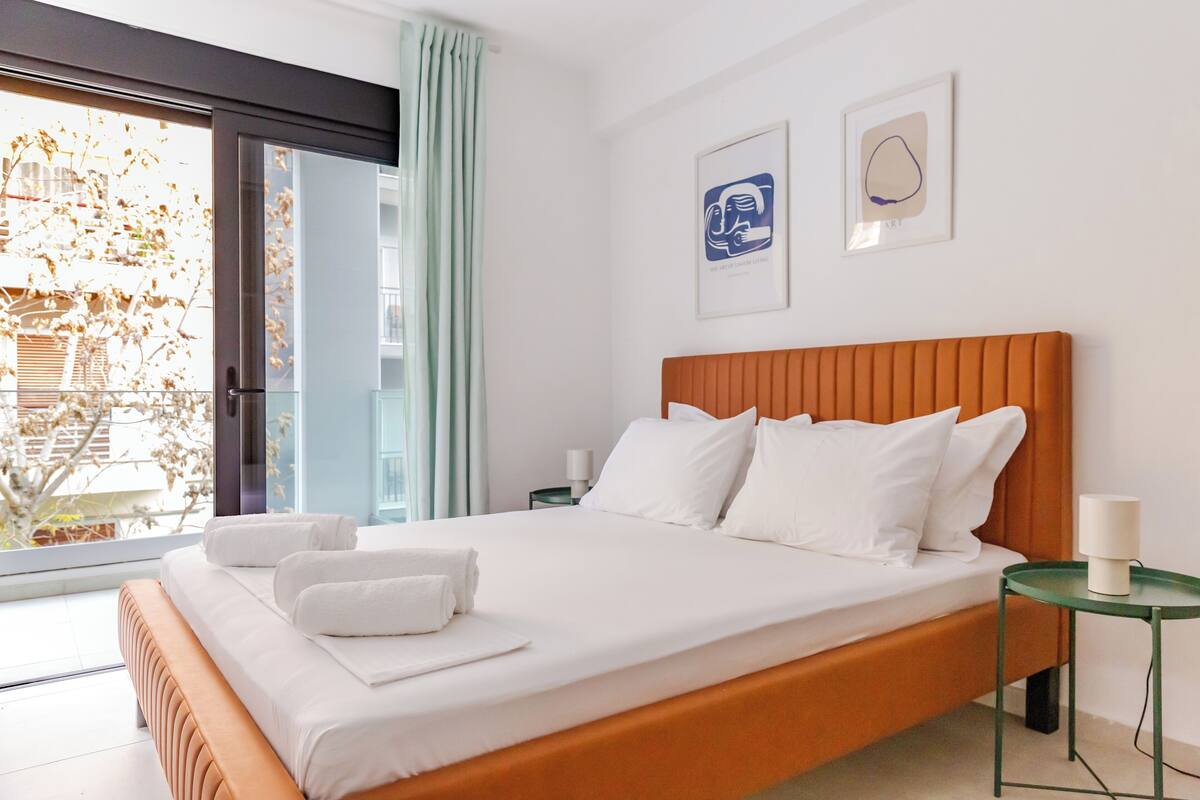 A modern hotel room with a large bed, a green side table, and two framed artworks on the wall.