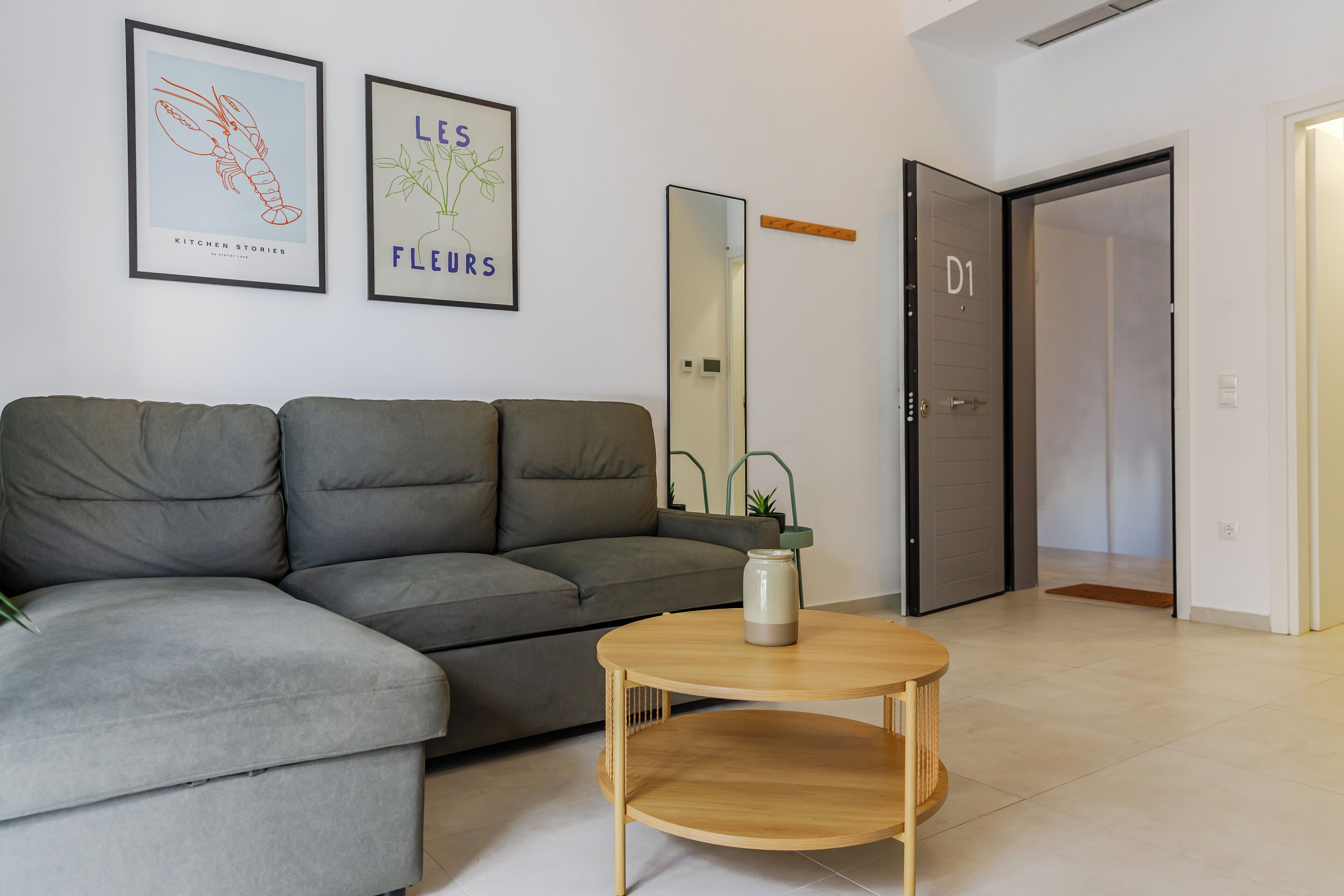 A modern living room with a grey sectional sofa, a round wooden coffee table, and two framed wall art pieces.