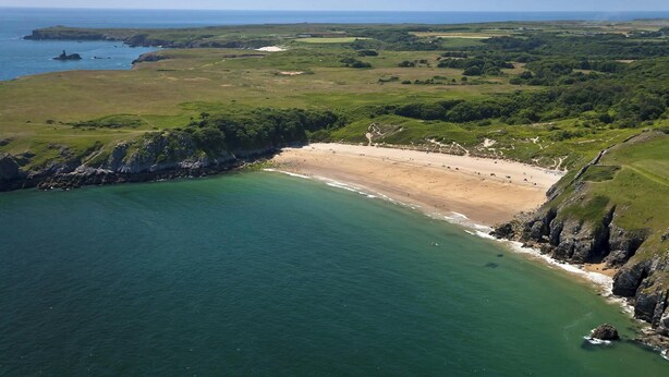 An aerial view of a coastal area with a beach, cliffs, and a clear sky.