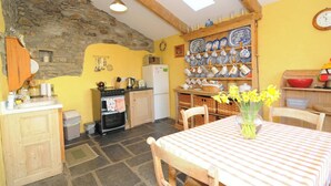 A kitchen with a stone wall, wooden beams, a yellow wall, a clock, and a table with a vase of flowers.