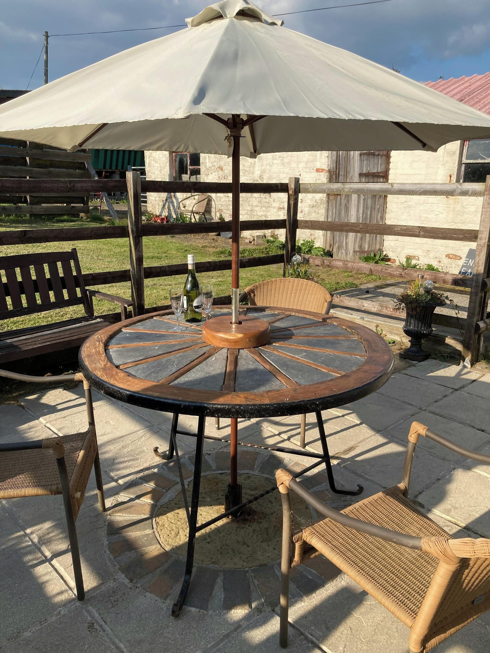 Et rundt udendørs bord med metalstel, omgivet af fletstole, under en stor parasol.