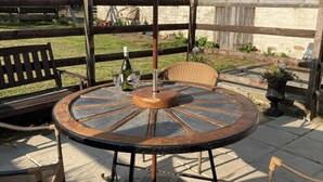 A round outdoor table with a metal frame, surrounded by wicker chairs, under a large umbrella.