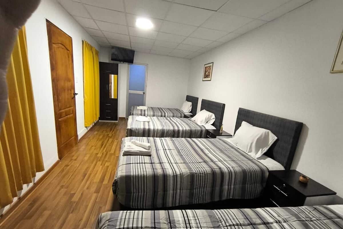 Ein Hotelzimmer mit drei Betten, Holzboden und einem Flur mit Türen.