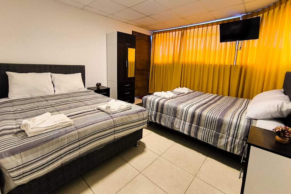 Ein Hotelzimmer mit zwei Betten, einem an der Wand befestigten Fernseher und einer Tür zu einem anderen Raum.