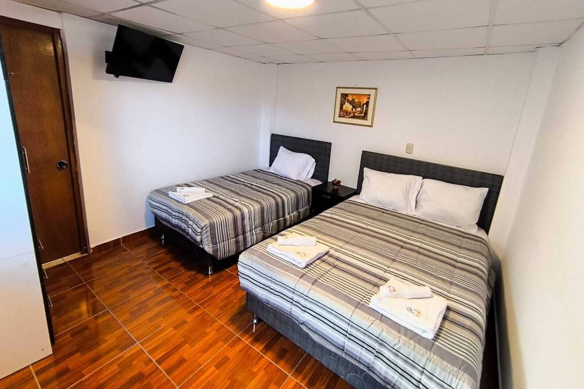 Ein Hotelzimmer mit zwei Betten, Holzboden, einem flachbildfernseher an der Wand und einem gerahmten Bild.