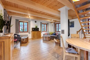A wooden-floored living room with a sofa, a dining table, and a staircase.