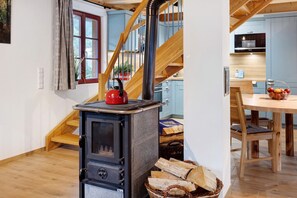 A kitchen with a wood-burning stove, a dining table with chairs, and a staircase with wooden railings. - Holiday Home 'Kornspeicher Untere Mühle' with Private Terrace and Wi-Fi (Königsfeld im Schwarzwald)