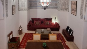 A room with a patterned ceiling, a red sofa, a wooden table, and a chandelier. - Beautiful 2-bedroom house "19th century Douiria" in Marrakech-with large terrace (Marrakech)