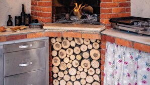 A rustic kitchen with a brick fireplace, wooden logs, and a metal cabinet.