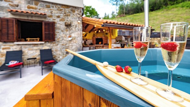 A poolside area with a wooden deck, lounge chairs, and a stone building in the background.