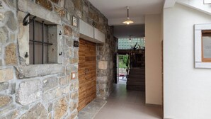 A hallway with stone walls, a wooden door, and a staircase leading to an upper level.