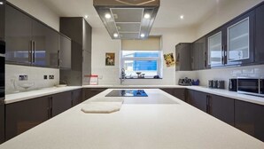 A modern kitchen with dark cabinets, a central island, and a window with a view. - The View Old Coastguard Cottage (Spanish Battery)