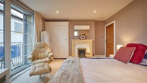 A bedroom with a large bed, a chair, a fireplace, and a view of the outside. - The View Old Coastguard Cottage (Spanish Battery)