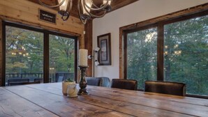 A wooden dining table with a candle centerpiece, large windows, and a 'Welcome Home' sign. - Chalet de l'aube | Spa (Sainte-Béatrix)