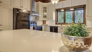 A kitchen with white cabinets, a stainless steel refrigerator, a wooden ceiling, and a large island with a plant. - Chalet de l'aube | Spa (Sainte-Béatrix)