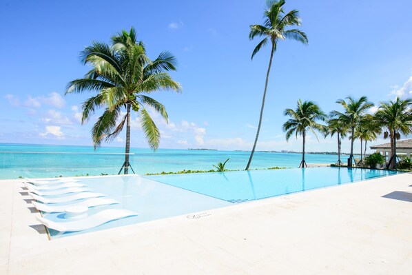 A pool with lounge chairs, palm trees, and a clear view of the ocean.