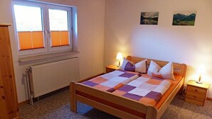 A bedroom with a wooden bed, two bedside tables, a radiator, and a window with blinds.